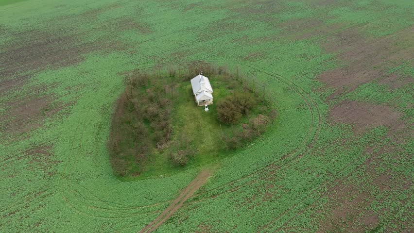 Aerial view of small white chapel in the middle of agricultural field by drone