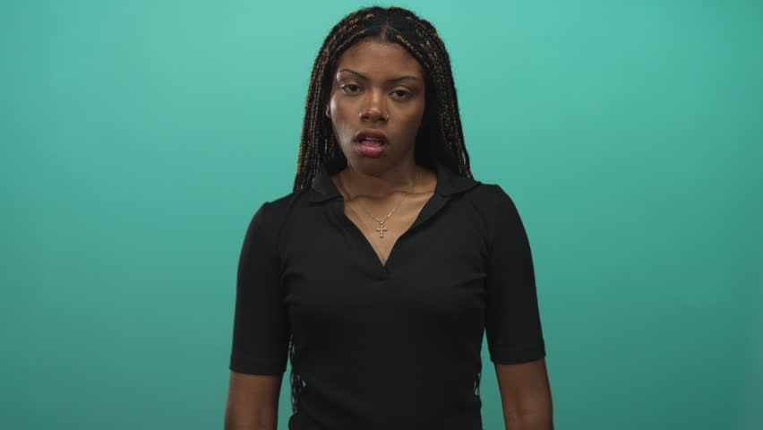 African american woman making ok sign with raised right hand, showing nose ring and braided hair in turquoise studio; indifference.