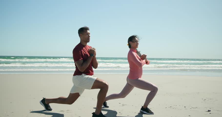 Diverse fitness partners stepping onto sand near ocean waves for warmup lunging, stretching muscles. Beach, workout, outdoor, athletic, harmony, endurance, vitality
