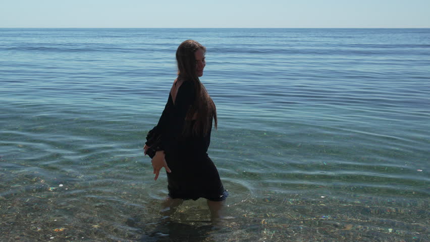 Woman, ocean, water, smiling woman in black dress enjoying clear shallow sea on sunny day