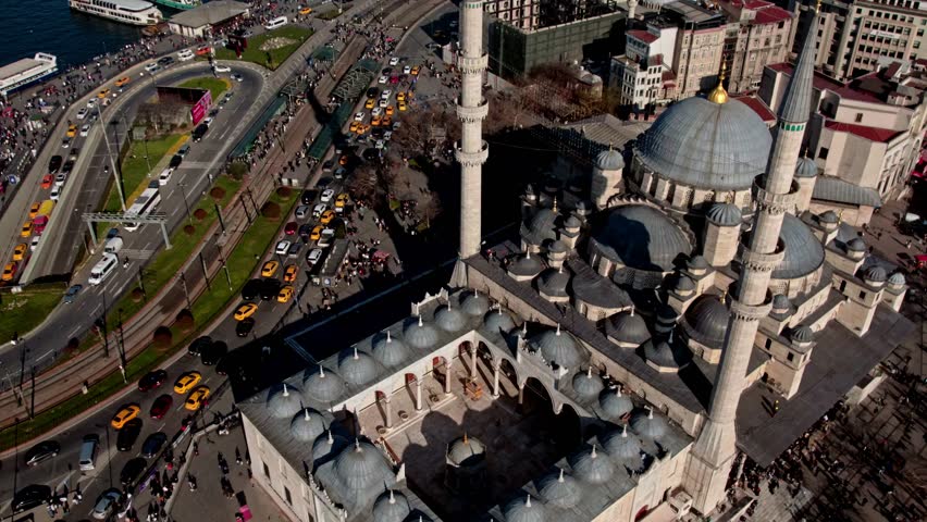 The New Mosque (Eminönü) stands at the center, with the Galata Bridge spanning the Bosphorus. Ferries, piers, dense urban fabric, and a misty atmosphere define the aerial city view.