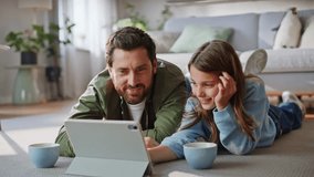 Father daughter watching tablet relaxing together apartment floor closeup. Happy bearded dad talking preteen girl browsing educational video pad computer home. Digital content family bonding leisure. - Powered by Shutterstock - Get 15% off with code: PIKWIZARD15