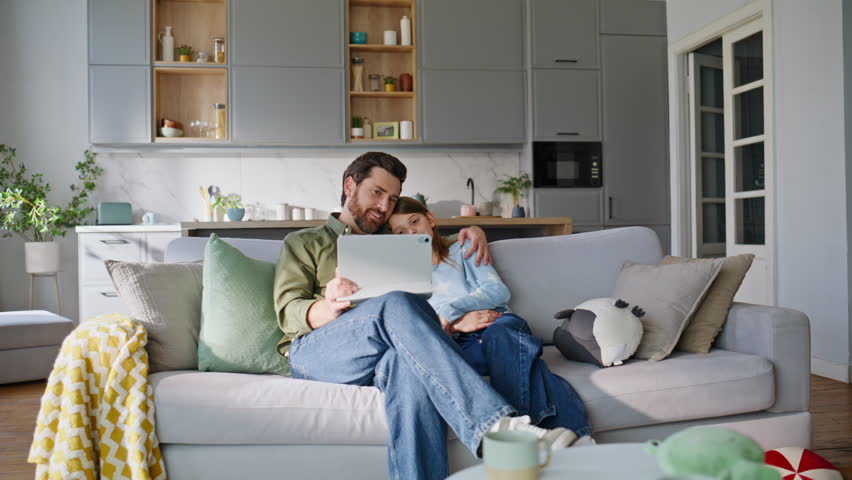 Bonding father daughter browsing tablet sitting comfortable home sofa. Happy carefree dad preteen girl watching online video relaxing together cozy living room couch. Casual family leisure concept.