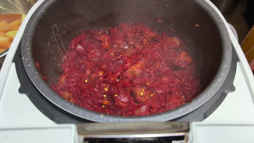 Stewing pieces of meat with typical set of vegetables in multi cooker bowl for following beetroot red borscht preparing, view close-up while approach
