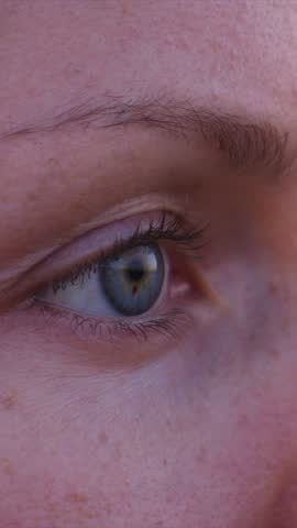Extreme close up of a young woman's blue eye and freckled skin with a beautiful lens flare effect reflecting from the warm golden hour sun, creating a thoughtful and nostalgic mood
