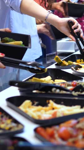 Close up view of people serving themselves with fresh vegetables and pasta at a self service buffet in a restaurant. Customers choosing a variety of dishes for a healthy lunch