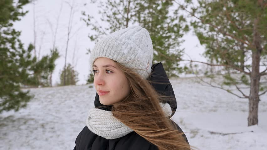 Portrait of a young beautiful girl in a hat with long hair on a snowy winter day