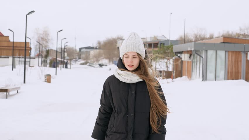 Portrait of a young beautiful girl in a hat with long hair on a snowy winter day