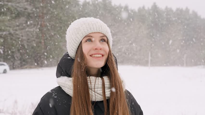 Portrait of a young beautiful girl in a hat with long hair on a snowy winter day