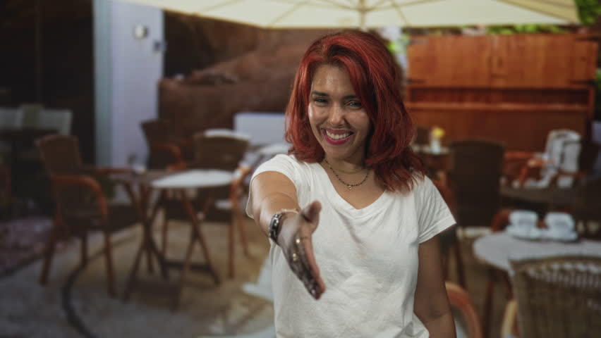 Woman offering a handshake with outstretched hand toward camera in restaurant building, smiling and inviting connection; welcoming warmth.