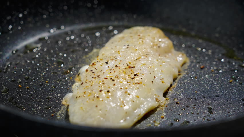 Frying white fish fillets. Frying hake fillets in a hot pan Sizzling pan oil and fish fillet searing, closeup of raw white fish placed in hot skillet with bubbling butter. Selective focus