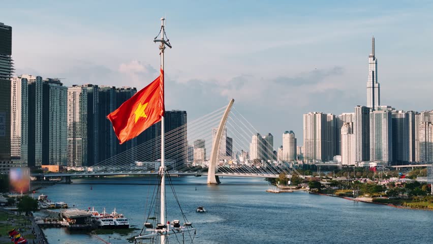 Vietnamese flag waving with ho chi minh city skyline and saigon river in the background.