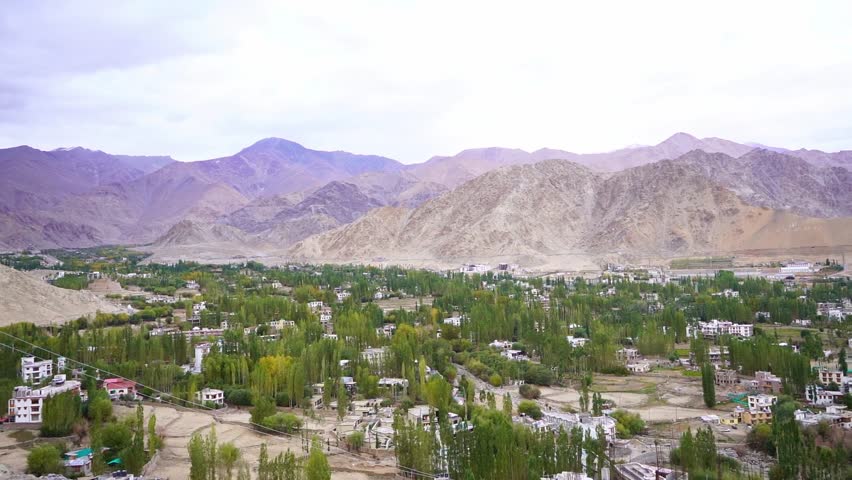 Scenic elevated view of Leh town in Ladakh, India, seen from the top of surrounding mountains. Beautiful Himalayan landscape with houses spread across the valley under clear blue sky. Iconic view of the remote Himalayan town with dramatic mountains, rugged terrain, and peaceful high-altitude scenery.