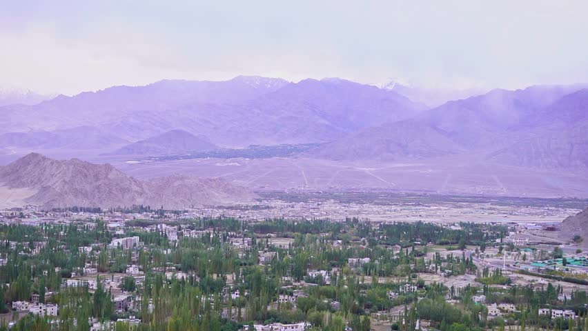 Scenic elevated view of Leh town in Ladakh, India, seen from the top of surrounding mountains. Beautiful Himalayan landscape with houses spread across the valley under clear blue sky. Iconic view of the remote Himalayan town with dramatic mountains, rugged terrain, and peaceful high-altitude scenery.