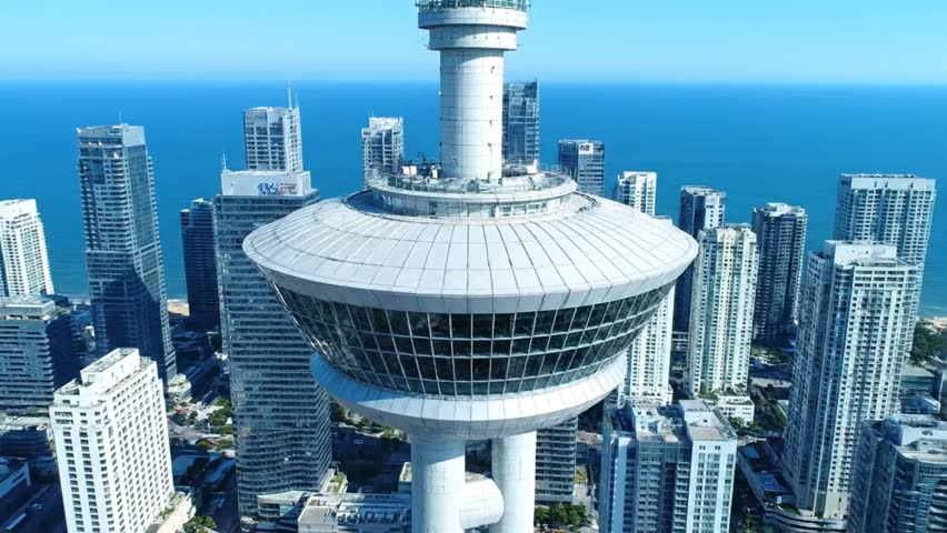 Aerial view of white observation tower over modern city skyline with blue ocean background