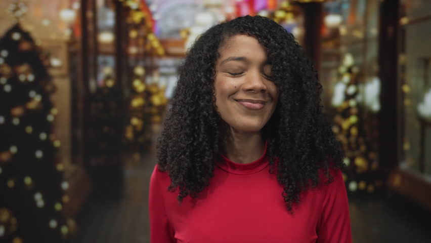 African american woman in red top smiling and finger to lips for silence on street; mystery intrigue.