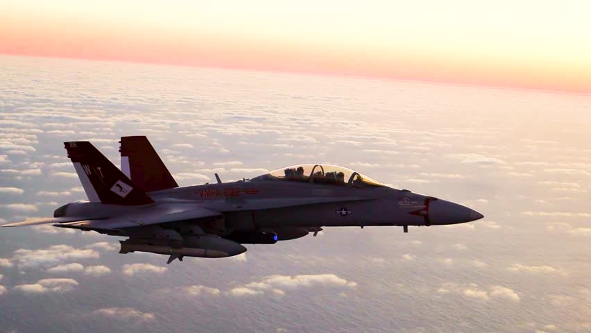 US Navy FA-18 fighter jet flying above clouds during dramatic sunset high altitude patrol mission.