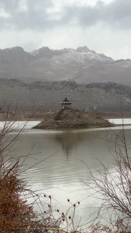 Serene lake scene with boat snow capped mountains and traditional pagoda style structures on small islands
