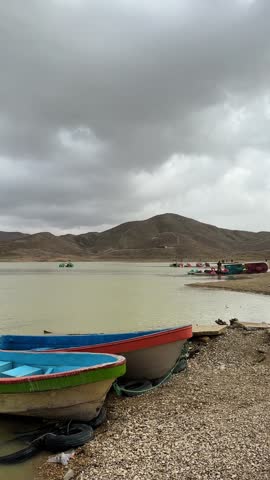 Panoramic view of small boats on a lake with mountains under a cloudy sky