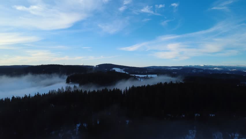 A cinematic drone aerial view of winter fog inversion over the Black Forest hills at sunrise. Misty clouds cover valleys while clear horizon and mountain silhouettes create dramatic atmospheric landscape scenery.