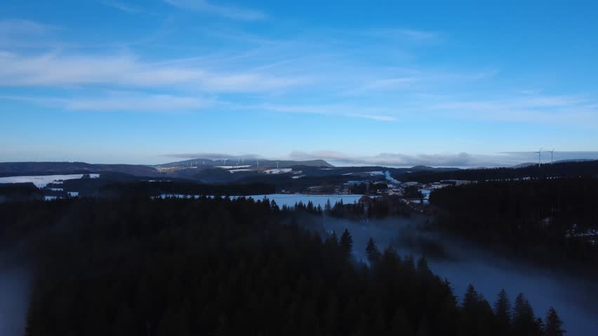 A cinematic drone aerial view of winter fog inversion over the Black Forest hills at sunrise. Misty clouds cover valleys while clear horizon and mountain silhouettes create dramatic atmospheric landscape scenery.