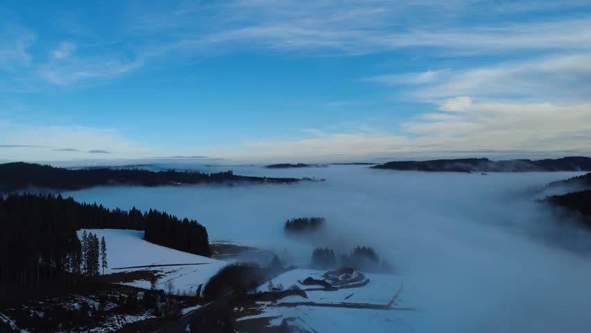 A cinematic drone aerial view of winter fog inversion over the Black Forest hills at sunrise. Misty clouds cover valleys while clear horizon and mountain silhouettes create dramatic atmospheric landscape scenery.