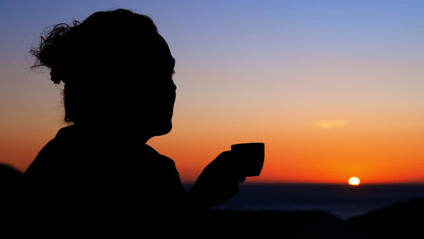 Silhouette of a woman enjoying coffee at sunset. Woman