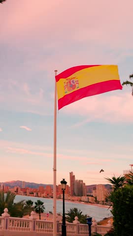 Spanish flag waving in the wind over benidorm cityscape at sunset