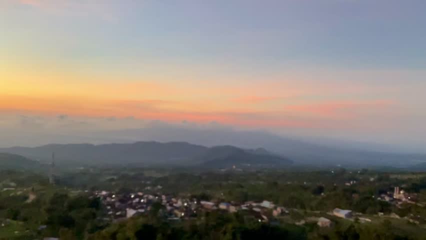 A breathtaking cinematic sunrise pans across a misty valley, revealing silhouetted volcanic peaks and a quiet mountain village under a vibrant orange and purple sky.