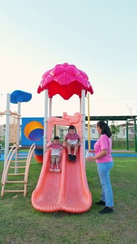 A woman is standing in front of a pink slide with two children on it