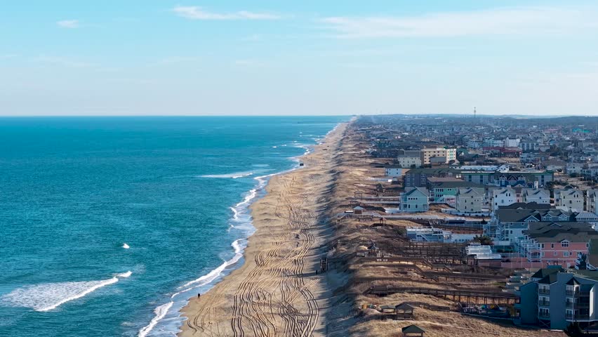Kill Devil Hills, North Carolina, aerial cinematic video of the Atlantic coastline featuring sandy beaches, vacation homes, and the expansive Outer Banks landscape.