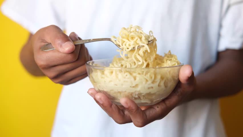 Close up of person holding bowl of instant noodles with fork, eating noodles