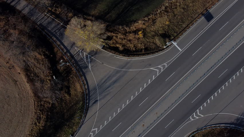 Cars driving along highway on autumn sunny day. Automobile road with white markings between agricultural fields. View of cars driving on paved road. Automobile vehicles. Top view. Aerial drone view.