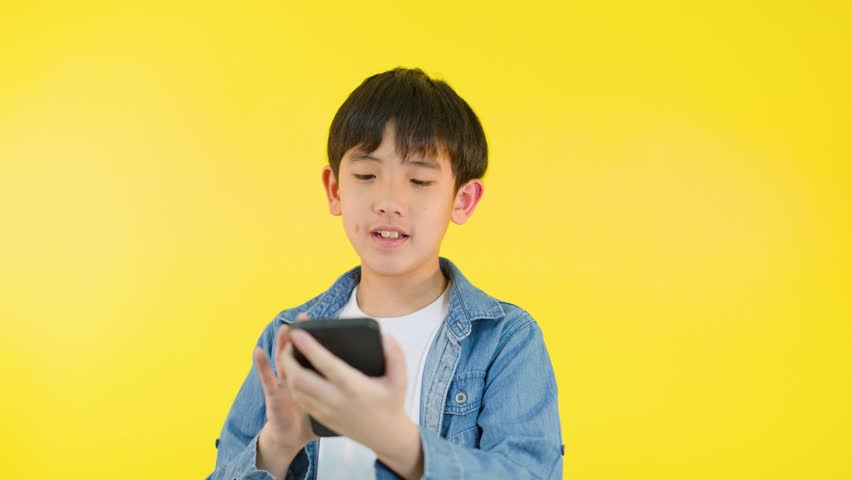 Smiling boy in denim shirt talks on smartphone against bright yellow background, cheerful mood.