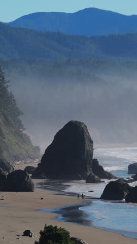 Wide coastal view of rocky Oregon Coast beach with sea stacks, ocean waves and forested cliffs. Natural light, fresh air and calm atmosphere showing wild Pacific shoreline.