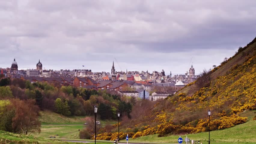View of Edinburgh from Arthur’s Seat on a cloudy day, showing historic buildings, rolling hills, and the urban cityscape below.