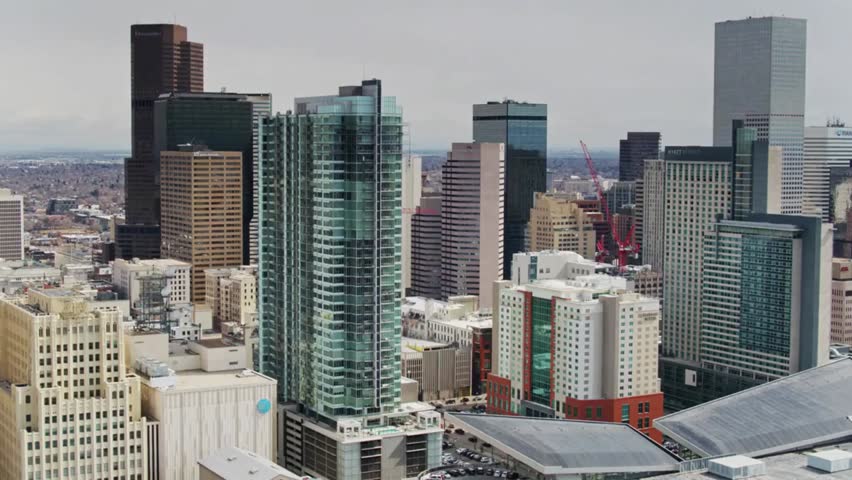 Daytime aerial view of Denver downtown skyline, featuring modern city buildings set against clear skies and distant mountains.