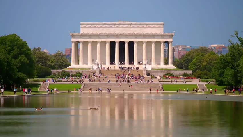 The Lincoln Memorial reflecting in the Reflecting Pool on a bright summer day, framed by blue sky and historic surroundings.