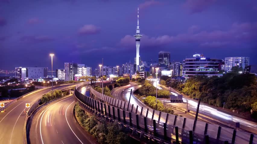 Auckland city skyline at night with traffic on the highway and Sky Tower, capturing vibrant urban lights, cityscape, and nighttime motion.