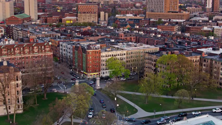 Aerial view of a Boston neighborhood with classic brick buildings, tree-lined streets, and urban residential charm under clear daylight skies.