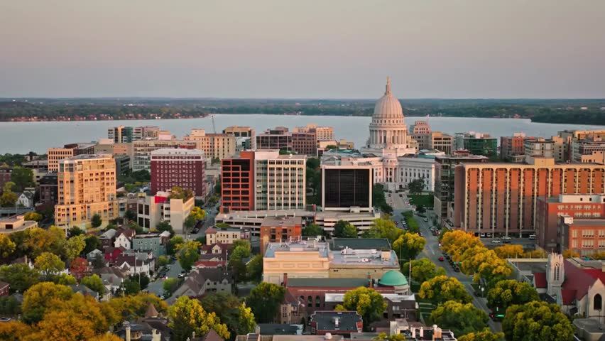 Aerial view of Madison, Wisconsin skyline featuring the Wisconsin State Capitol illuminated by warm sunset light over the city.