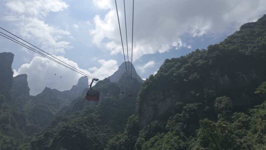 Cable cars glide above steep forested slopes at Tianmen Mountain Zhangjiajie China, ascending tourist pov