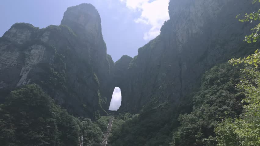 Natural rock arch framed by towering cliffs at Tianmen Mountain Zhangjiajie China, upward angled background