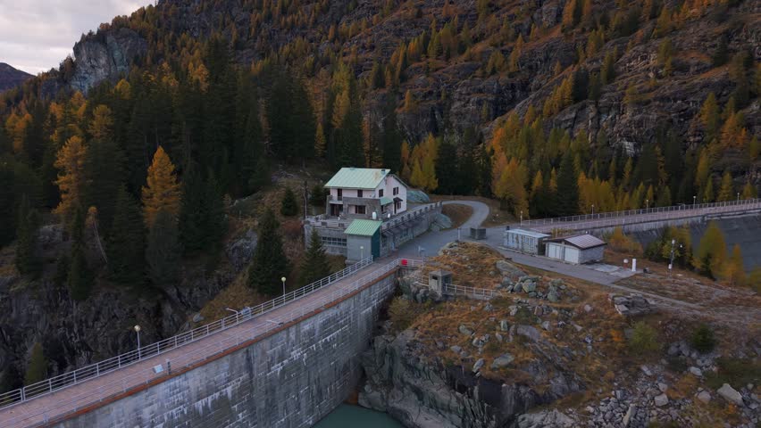 Drone view of a reservoir and hydroelectric dam in an alpine valley during fall season in Italy. Aerial backward