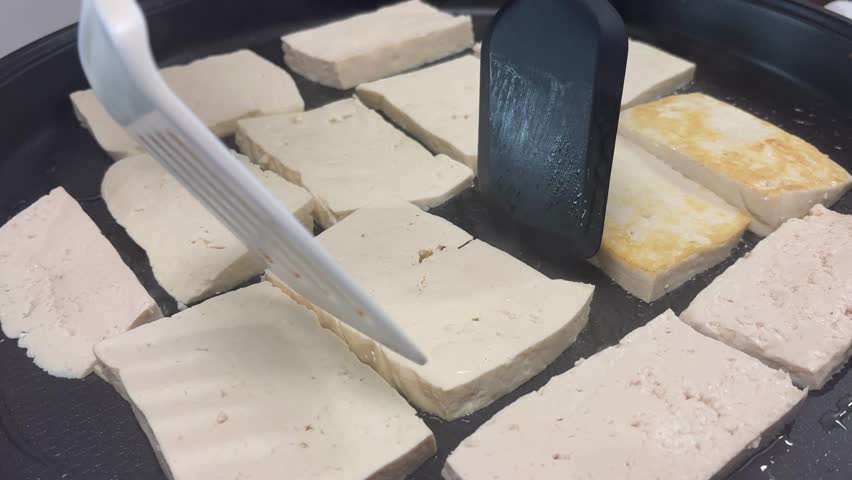 Sizzling tofu slices being fried to perfection on a flat griddle, Korean side dish Dubu-jeon