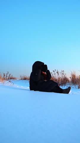 Woman lying down in snow on coastal dune landscape. Side view of a person in black winter gear lying on a snow covered hill at the beach.