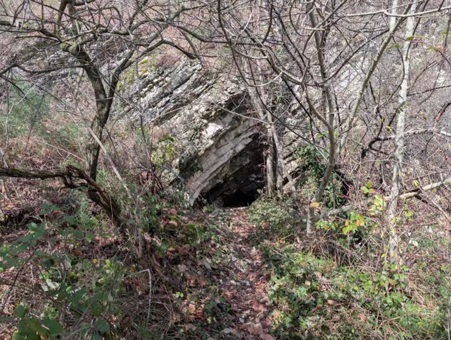 Entrance to a natural cave within a layered rock formation. The tilted and fractured rocks reveal ancient geological processes.