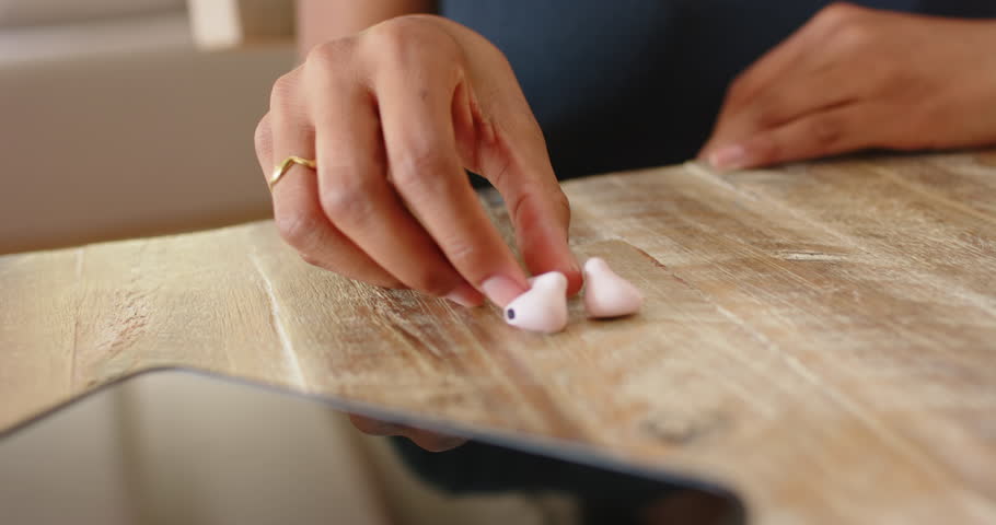 African American woman seeing earbuds at home, grabbing, inserting earbud, phone nearby for music. Wireless, audio, gadget, tech, modern, lounge, listening