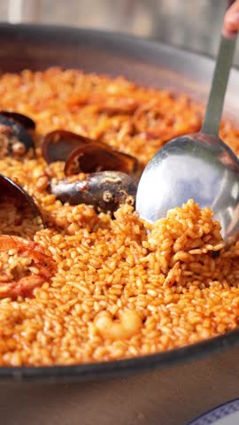 A person is scooping food out of a large bowl. The bowl is filled with rice and shrimp