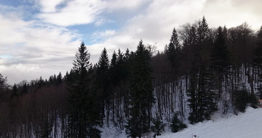 Aerial panorama video of ski slope in Hochficht Austria with skiers on snow covered piste surrounded by forest and dramatic winter clouds